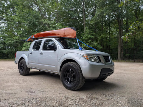 Truck with kayak secured using Heavy Duty 1 Inch Ratchet Tie Down Strap 6 Ft Long, 900 Lbs Break Strength, in wooded area