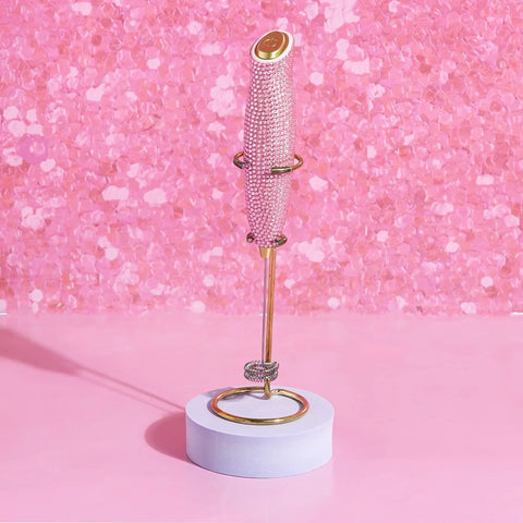 Electric Rhinestone Handheld Milk Frother With Double Coil Whisk And Gold Stand Pink Battery Powered Portable Frother For Lattes Cappuccinos And More Fast Foaming In Under 30 Seconds Requires 2 AA Batteries Not Included shown upright on gold stand against pink background