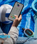 Person using phone app to customize RGB lights on a Portable Bluetooth Speaker Waterproof IP55 at a beach with sports gear.