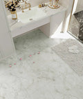 Bathroom scene showcasing marble flooring tiles with rose petals, white countertop, and plush rug beside a glass shower.