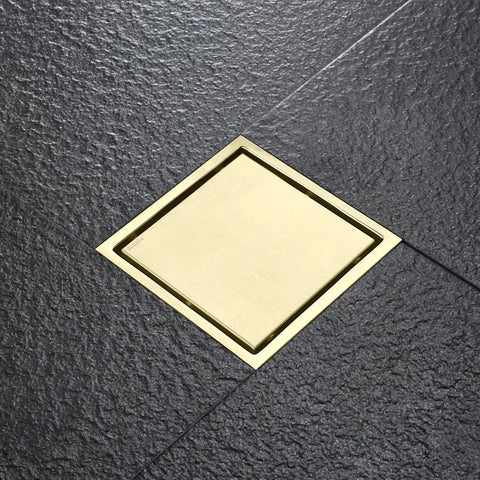 Top Shelf Four Inch Square Shower Drain With Flange Removable Grate Brushed Gold Stainless Steel Hair Catcher on tiled floor.