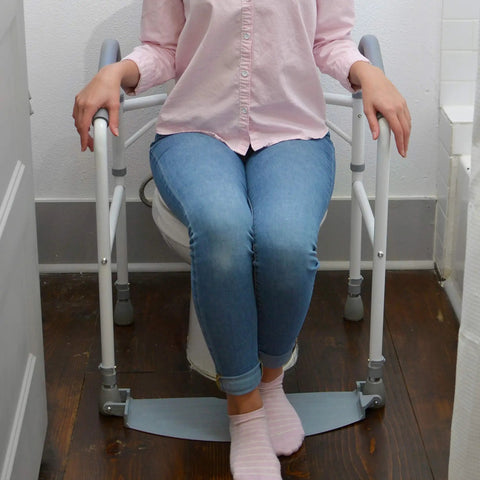 Woman seated using Hassel Free Folding Toilet Safety Frame And Super Solid Portable Bathroom Handrail With Comfy Foam Armrests.