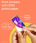 Hands peeling 2x3 sticky back print from Ivy 2 Mini Photo Printer For IPhone And Android Zero Ink ZINK Tech Print Sticky Back Photos On The Go No Ink Needed Quick Colorful Prints In Pure White Finish.