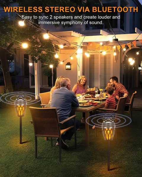 Family enjoying dinner on patio with 2 Pack Outdoor Bluetooth Speakers With LED Flame Flickers, IP5X Waterproof Lantern Speakers in garden