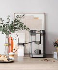 Fully Automatic Espresso Machine With Built In Grinder And Dual Boilers brews cappuccino next to coffee and dessert on a kitchen counter.