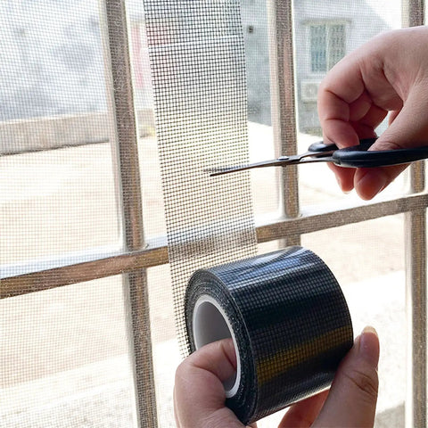 Person using scissors to cut Heavy Duty Window Screen Repair Tape And Mesh Patch Kit 2 Inches By 16 Feet Long Black adhesive strip.