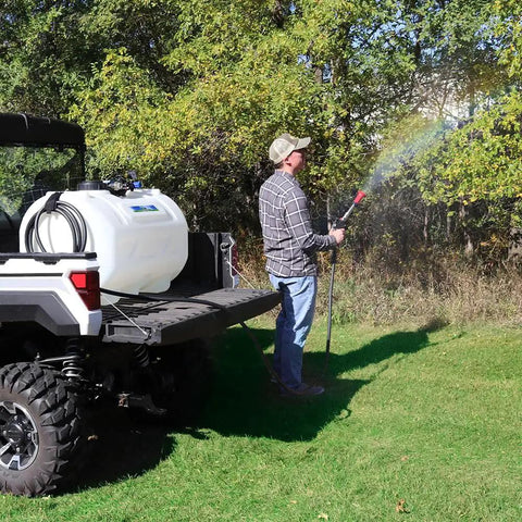 Person using Beefy 4.0 GPM 12V Diaphragm Pump with Half Inch NPT Ports to spray in a field, attached to a utility vehicle.