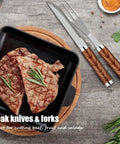 Grilled steak in a cast iron pan with wooden-handled steak knife and fork on a stone surface.