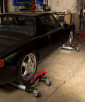 Heavy Duty 1500 Lb Wheel Dolly Rock Solid Ratchet Lift With Big Pedal That Keeps Toes Safe and Outboard Locking Casters under black car tires in garage.