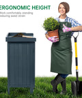Woman standing beside Outdoor Storage Cabinet With Potting Bench And Metal Tabletop For Garden And Patio, holding plant and shovel