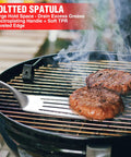 Grilling burgers with spatula from heavy duty BBQ tool set with premium stainless steel spatula fork brush and tongs for grilling lovers outdoors a top notch gift idea for men and women who live for the grill.
