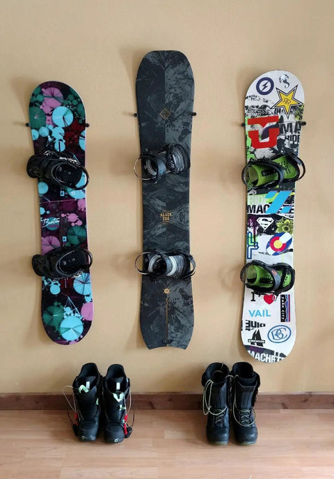Minimalist Snowboard Wall Mount Display Rack Featuring Felt Padded Arms And Durable Rubber Grip To Stash Your Sick Ride Securely In Garage Or Home Studio And Recreation Room with three mounted snowboards and boots.