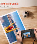 Person holding camera with photo print on table showing colorful landscape and person in yellow jacket, titled 'Print Vivid Colors'.