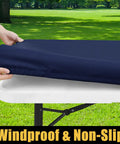 Hands fitting a navy waterproof elastic tablecloth with elastic edge onto a 6-foot table for outdoor use, spillproof windproof