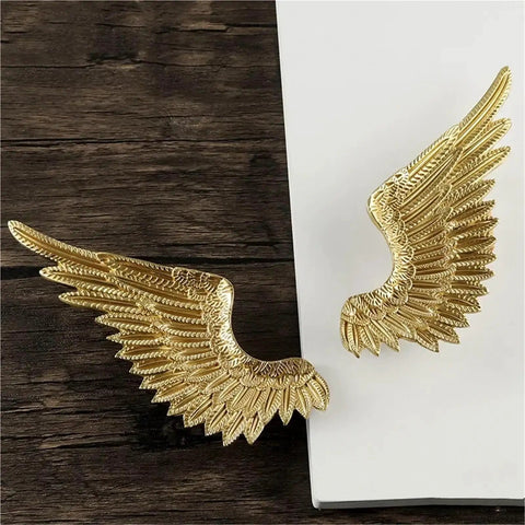 Heavy Duty Solid Brass Wardrobe Handles Featuring Slick Matte Gold Angel Wing Design And Badass Cabinet Knobs close-up of gold angel wing handles on wooden surface