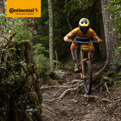 Mountain biker navigating forest trail, wearing helmet and orange suit. Image tag reads 'Continental The Future in Motion.'