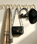 Heavy Duty Gold Wall Mounted Coat Rack With Sculpted Wavy Hooks hanging a black bag, scarf, headphones, and cap.