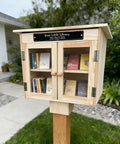 Outdoor Little Library Box with stand and nameplate, clear doors, situated in garden, natural wood finish, books visible inside
