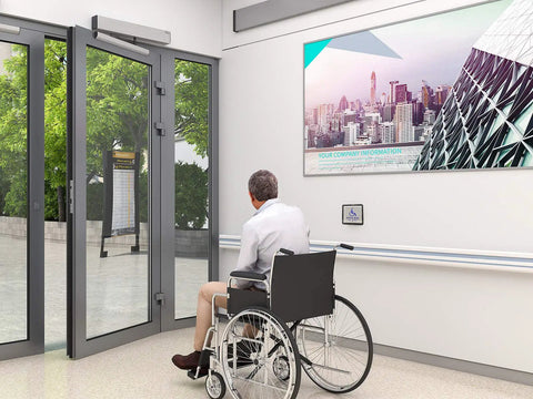 Wireless Swing Door Operator With Square Handicap Push Buttons And Built Tough Stainless Steel Electric Strike For Commercial Entrances, opening towards a wheelchair user.