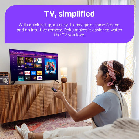 Woman using remote with 55 Inch QLED Smart TV displaying Roku interface in cozy living room setting.