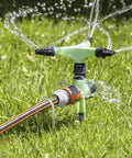 Garden sprinkler system in operation on green lawn with visible hoses and water spray, suitable for irrigation setup.