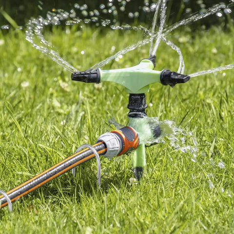 Garden sprinkler system in operation on green lawn with visible hoses and water spray, suitable for irrigation setup.