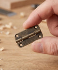 Hand holding small antique cabinet hinge with rounded corners, four-hole vertical iron construction for cupboards and bookcases.
