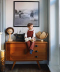 Child sitting on a mid-century modern cabinet, holding a teddy bear, with matte black cabinet drawer pulls visible.