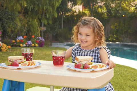 Child enjoying a meal at a Six Seat Kids Picnic Table with Umbrella, showcasing outdoor use with snacks and drinks, multi-color design.