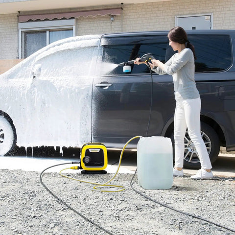 Woman using water suction hose with filter for electric pressure washers to clean car, hose connected to pump and water tank