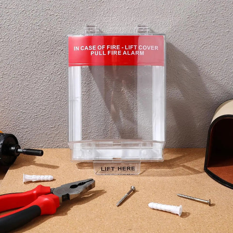 Straight Up Tough Fire Alarm Pull Station Cover with red warning label, clear plastic, installed with tools on table.