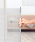 Hand operating a gray retractable baby and pet safety gate, 54 inch wide, 34 inch tall, for doorways and stairs, indoor and outdoor use.