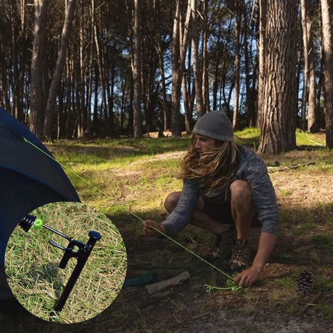 Person using Eight Pack Heavy Duty Tent Stakes 12 Inch Steel Pegs to secure a tent in a forested, windy campsite setting