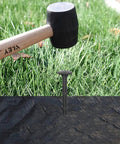 80 Pack Plastic Lawn Stakes Six Inch Ground Anchors Spikes Heavy Duty being hammered into weed fabric in a garden setup