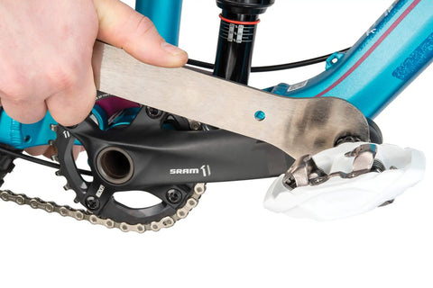 Close-up of All In One Chain Whip And Pedal Wrench For Bike Maintenance, 10.75 Inch Steel Tool in use on a bike pedal.
