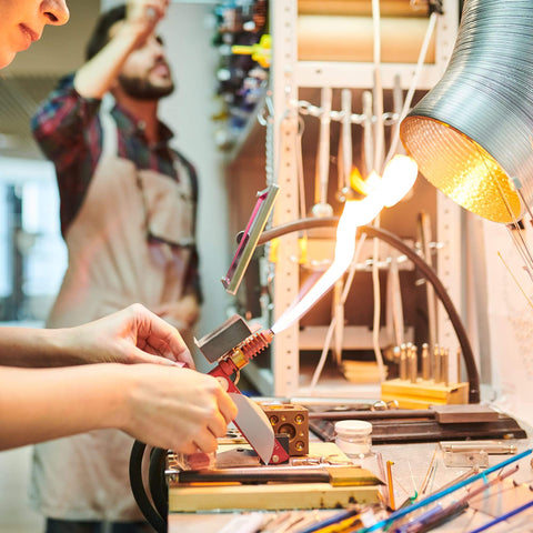 Person using flame torch in lab setting with shelves and tools in background