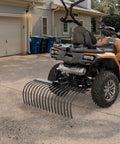 Tow Behind Landscape Rake With 48 Inch Working Width, 17 Steel Tines, 2 Inch Receiver, attached to an ATV for lawn cleanup.
