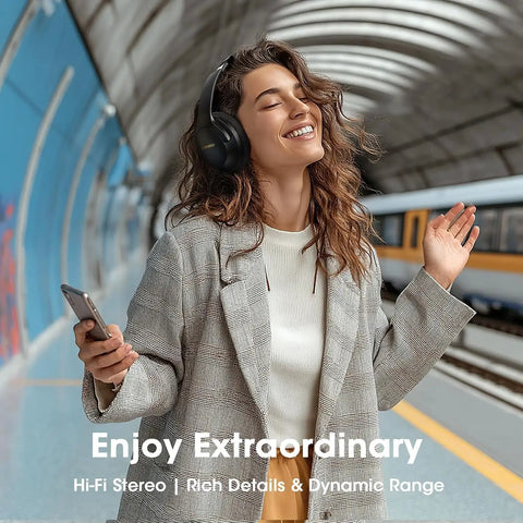 Smiling woman wearing over ear wireless headphones with 80 hour battery life, deep bass EQ and ENC mic, in train station