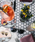 Hexagonal table with Dope 6 Piece Diamond Painting Coaster Set With Holder For Drinks And Coffee Tables, flowers, and glasses of cocktails.