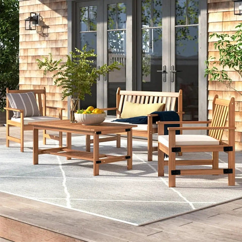 Outdoor patio set with wooden furniture and grey rug on a deck, featuring chairs and a table with potted plants and cushions.