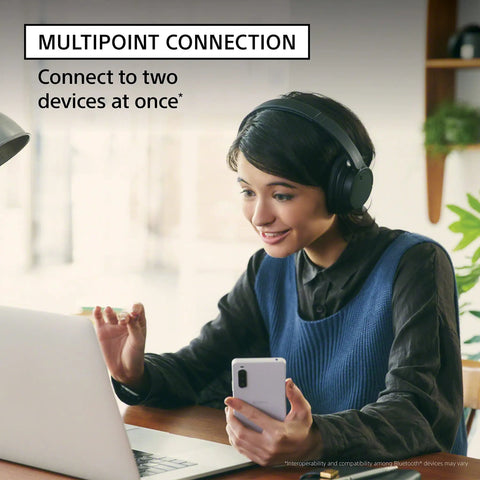 Woman using laptop and phone with lightweight noise cancelling wireless headphones with Alexa built in ultra comfortable over ear fit at 192g dual noise sensor tech for crisp calls Bluetooth five point zero long battery life and microphone for clear voice, demonstrating multipoint connection feature.
