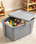 Kickass 30 Gallon Heavy Duty Plastic Storage Bin With Secure Snap Lid For Garage Organization Seasonal Gear Sorting And Everyday Essentials In Matte Gray Finish filled with toys and blocks on a rug.