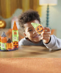 Child smiling while holding neon block, building a mini haunted house with 24 Piece Halloween Magnetic Building Tiles For Kids.
