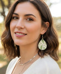 Woman wearing a teardrop earring with a fern design, part of the Unfinished Wooden Earring Blanks Set With Teardrop, Circle, Leaf, And Diamond Shapes, 60 Blanks Plus 60 Earring Hooks And 60 Jump Rings For DIY Jewelry Making.