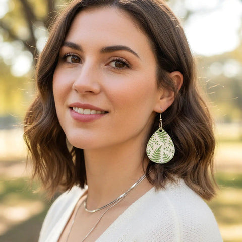 Woman wearing a teardrop earring with a fern design, part of the Unfinished Wooden Earring Blanks Set With Teardrop, Circle, Leaf, And Diamond Shapes, 60 Blanks Plus 60 Earring Hooks And 60 Jump Rings For DIY Jewelry Making.