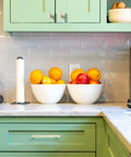 Modern kitchen with green cabinets, marble countertop, bowls of fruit, and a coffee maker.