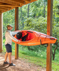 Man using Heavy Duty Swivel Kayak Rack For Garage Walls That Folds Flat Saves Floor Space to store an orange kayak.