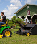 Man using 40 Inch Tow Behind Lawn Sweeper With Dethatcher And Hamper Windscreen attached to tractor for yard cleanup