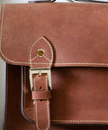 Close-up of a brown leather bag with a buckle and stitching details showing quality craftsmanship.