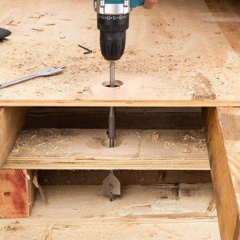 PINOZE 14-piece spade drill bit set; teal cordless drill drilling a hole in plywood on a workbench